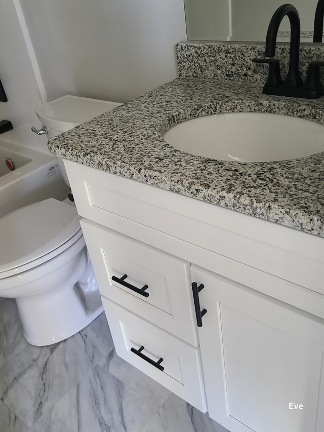 full bathroom featuring toilet, marble finish floor, a bath, and vanity