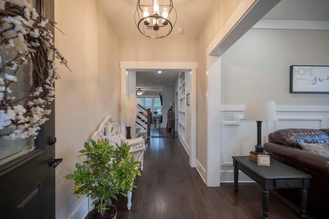 foyer with dark wood finished floors, an inviting chandelier, and a decorative wall