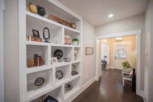 corridor with baseboards, built in shelves, dark wood-style floors, and a chandelier