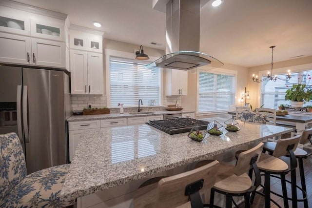 kitchen featuring a sink, stainless steel fridge, white cabinets, tasteful backsplash, and island range hood