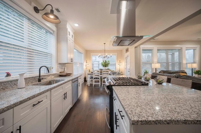 kitchen featuring light stone counters, appliances with stainless steel finishes, island range hood, white cabinets, and a sink