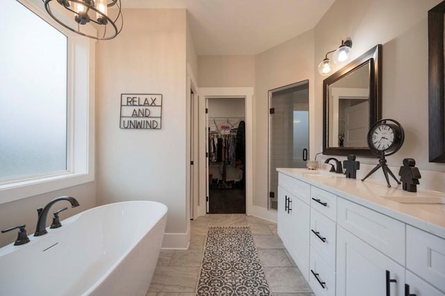 bathroom featuring double vanity, a freestanding tub, an inviting chandelier, a sink, and a walk in closet