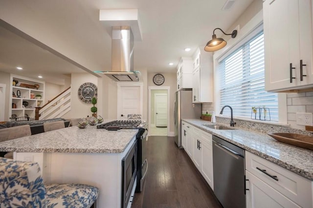 kitchen featuring light stone counters, range hood, stainless steel appliances, white cabinetry, and a sink