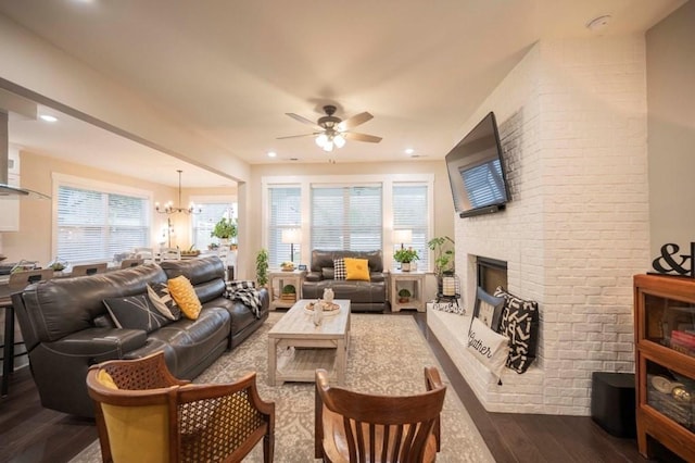 living area featuring a brick fireplace, recessed lighting, ceiling fan with notable chandelier, and dark wood-style flooring