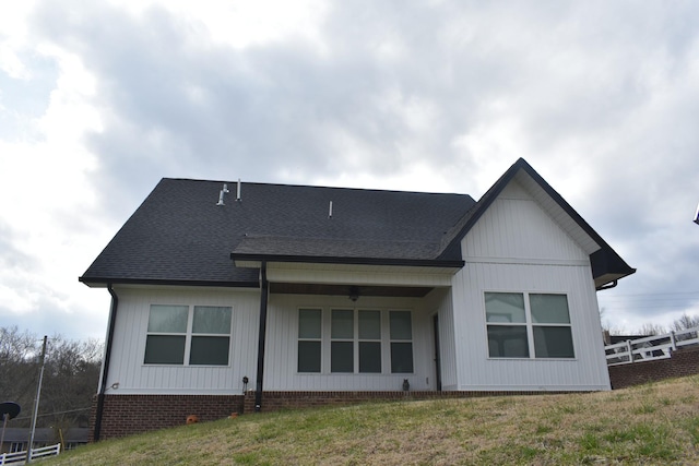 rear view of property featuring a lawn, roof with shingles, and ceiling fan