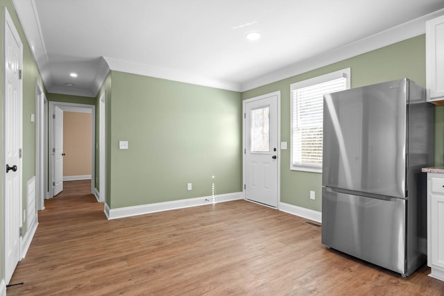 kitchen with white cabinets, ornamental molding, light hardwood / wood-style floors, and stainless steel fridge