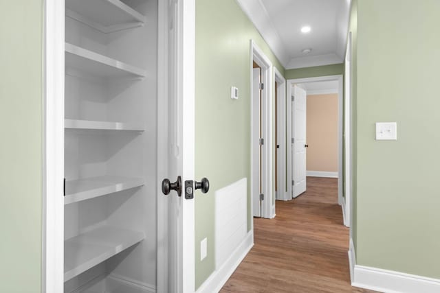 hallway featuring wood-type flooring, crown molding, and built in features