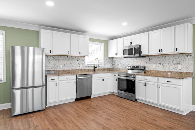 kitchen featuring appliances with stainless steel finishes, light hardwood / wood-style floors, dark stone counters, white cabinets, and sink