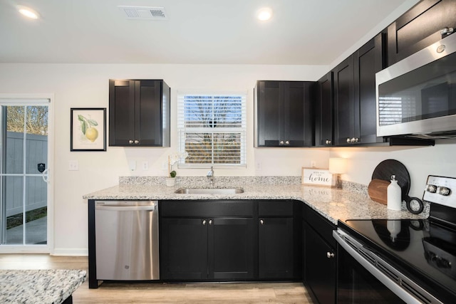 kitchen with light stone countertops, light wood-type flooring, stainless steel appliances, and sink