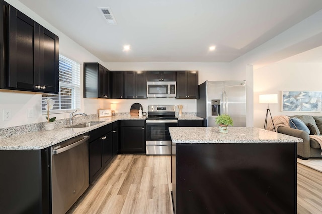 kitchen with appliances with stainless steel finishes, light stone counters, sink, a center island, and light hardwood / wood-style floors