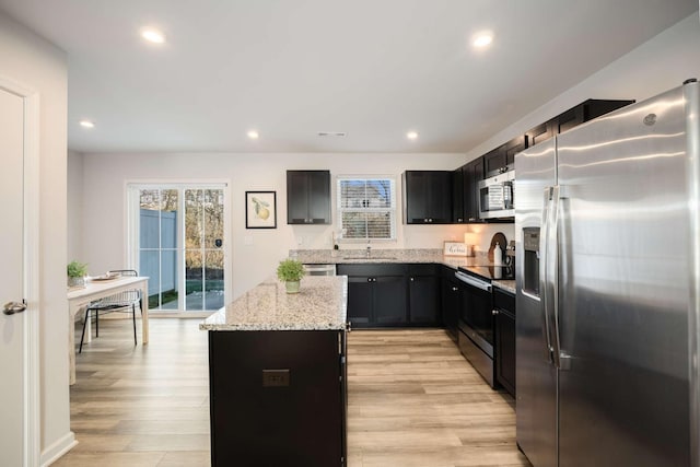 kitchen with appliances with stainless steel finishes, light stone counters, sink, a center island, and light hardwood / wood-style floors