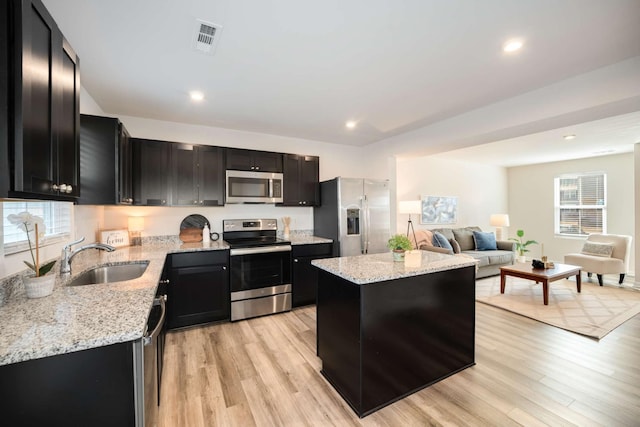 kitchen featuring a kitchen island, light wood-type flooring, light stone countertops, and appliances with stainless steel finishes