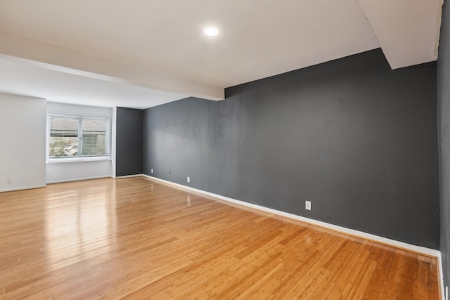 unfurnished room with beam ceiling and light hardwood / wood-style flooring