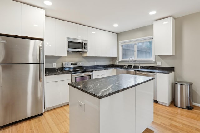 kitchen with white cabinets, a center island, stainless steel appliances, sink, and light wood-type flooring