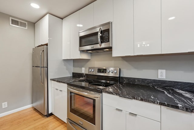 kitchen with light wood-type flooring, dark stone counters, stainless steel appliances, and white cabinetry