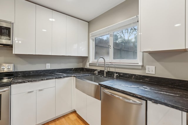 kitchen with sink, white cabinets, stainless steel appliances, and dark stone counters