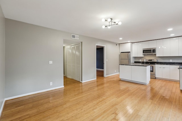 kitchen featuring white cabinets, a kitchen island, stainless steel appliances, a notable chandelier, and light hardwood / wood-style flooring