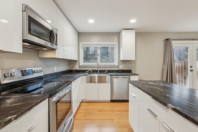 kitchen with light hardwood / wood-style floors, stainless steel appliances, dark stone countertops, white cabinets, and sink