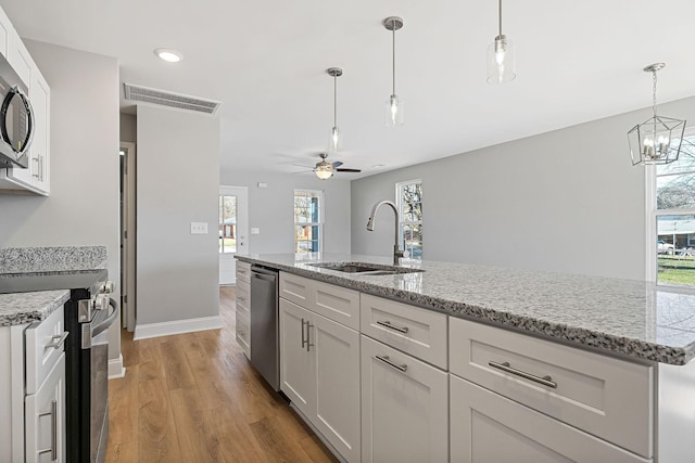 kitchen featuring white cabinets, ceiling fan with notable chandelier, sink, an island with sink, and appliances with stainless steel finishes