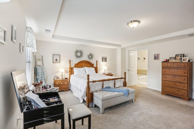 carpeted bedroom featuring a tray ceiling and ensuite bath