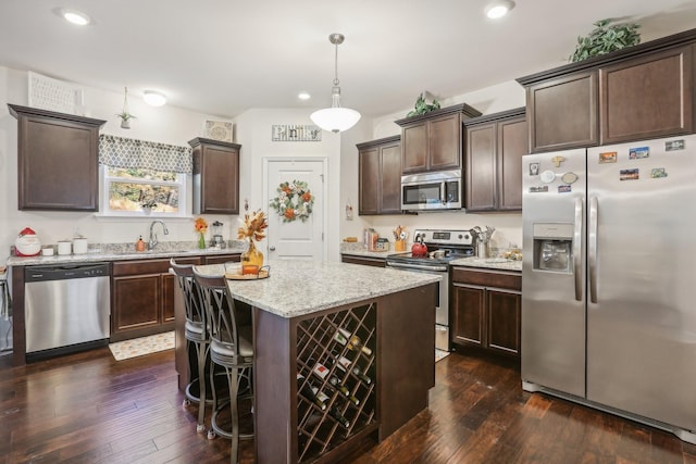 kitchen with a center island, sink, dark wood-type flooring, stainless steel appliances, and decorative light fixtures