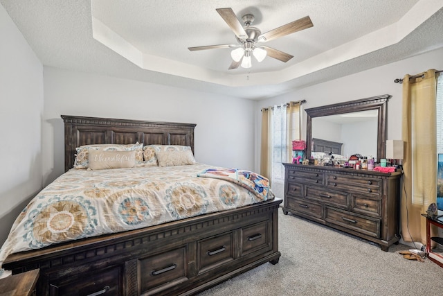 carpeted bedroom featuring a textured ceiling, a raised ceiling, and ceiling fan