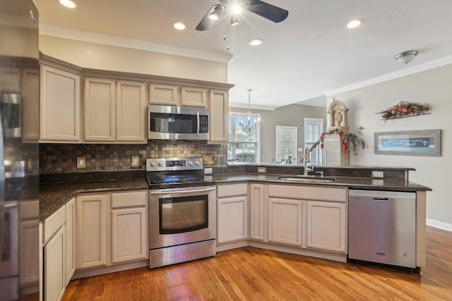 kitchen with kitchen peninsula, cream cabinets, stainless steel appliances, backsplash, and sink