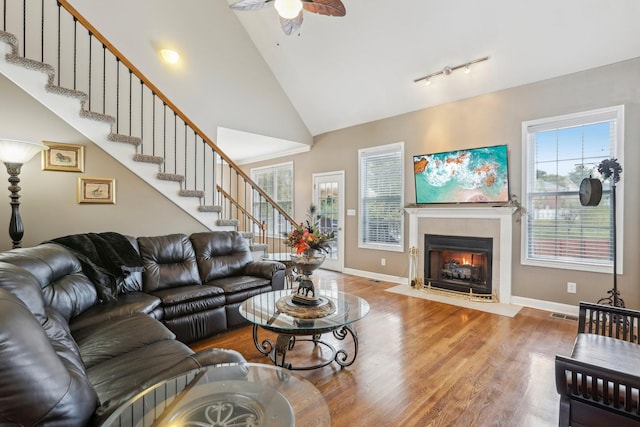 living room with a tiled fireplace, ceiling fan, high vaulted ceiling, and wood-type flooring