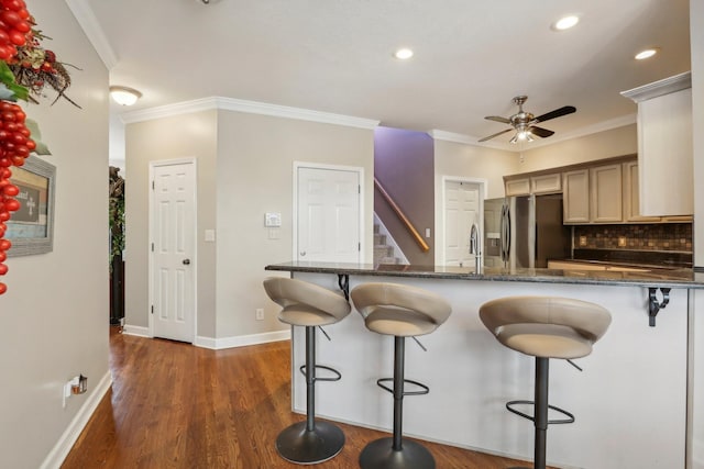 kitchen featuring dark stone counters, a kitchen bar, crown molding, and stainless steel refrigerator with ice dispenser