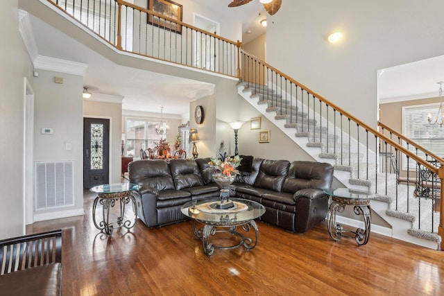 living room with ornamental molding, an inviting chandelier, a towering ceiling, and wood-type flooring