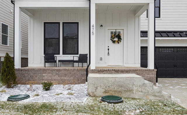 snow covered property entrance with covered porch and a garage