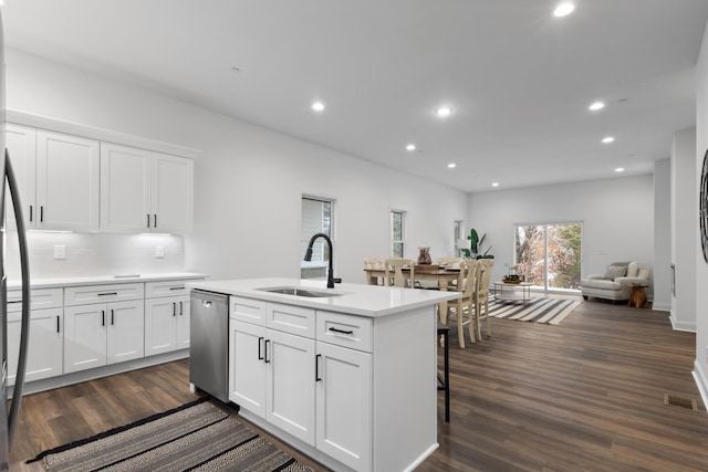 kitchen featuring dark wood-type flooring, white cabinets, sink, stainless steel dishwasher, and an island with sink