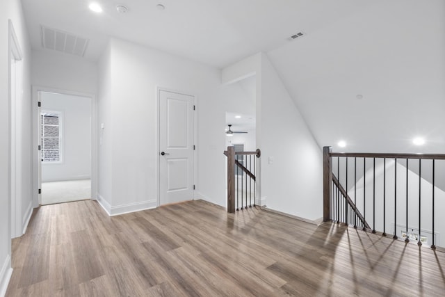 corridor with light wood-type flooring and vaulted ceiling