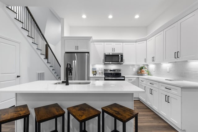 kitchen featuring a breakfast bar, a center island with sink, white cabinets, decorative backsplash, and stainless steel appliances