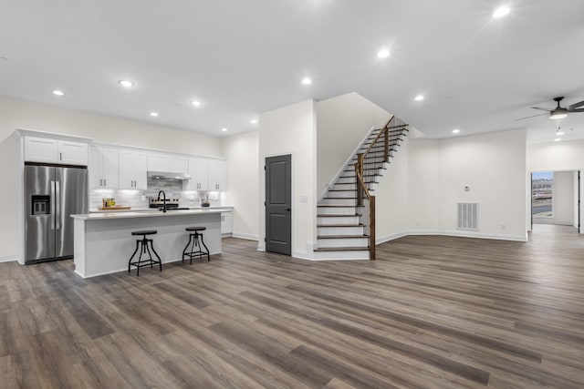 kitchen with sink, a kitchen breakfast bar, stainless steel refrigerator with ice dispenser, a kitchen island with sink, and white cabinets