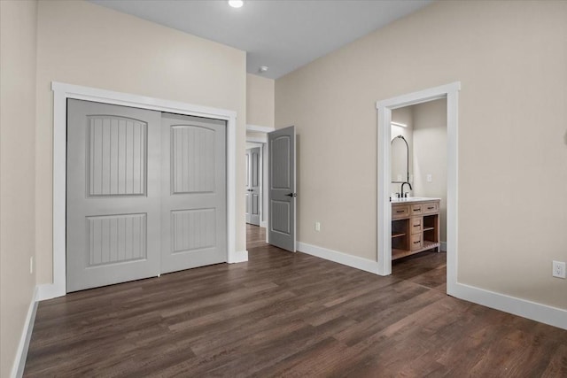 unfurnished bedroom with ensuite bathroom, dark wood-type flooring, a sink, baseboards, and a closet