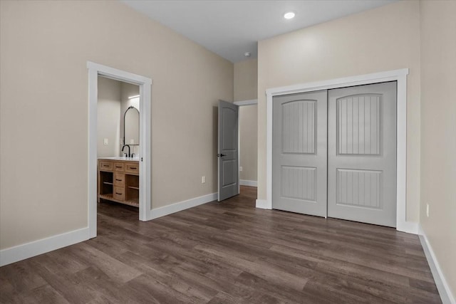 unfurnished bedroom featuring a closet, baseboards, ensuite bath, dark wood-style flooring, and a sink