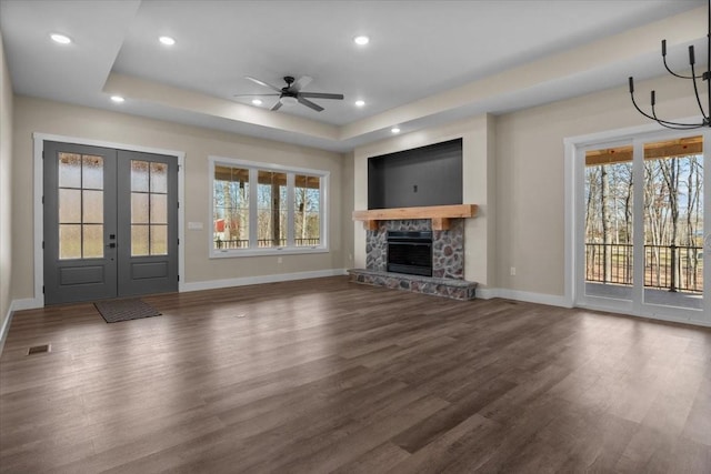 unfurnished living room featuring ceiling fan, a fireplace, a raised ceiling, dark wood-type flooring, and french doors