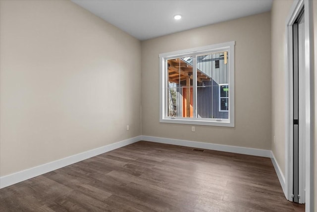 empty room with dark wood-style floors, visible vents, and baseboards