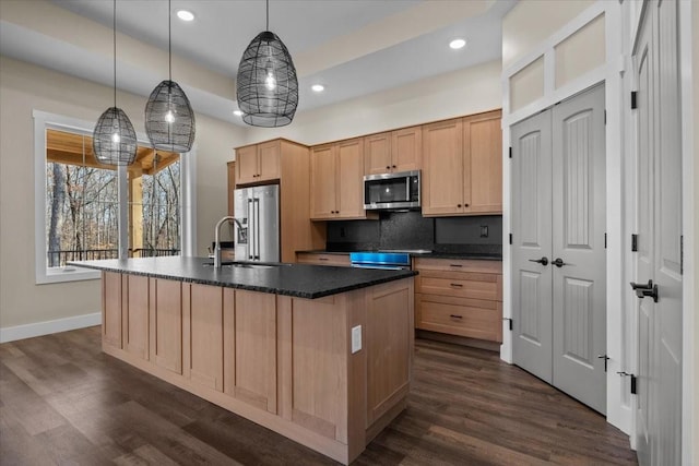 kitchen with decorative backsplash, dark wood finished floors, dark countertops, appliances with stainless steel finishes, and a sink