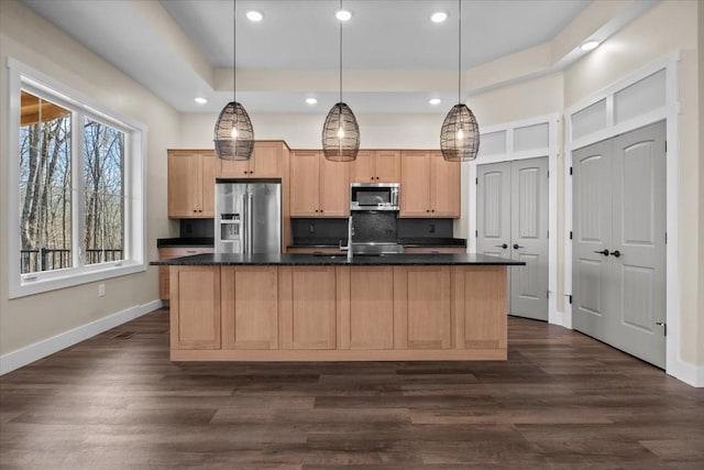 kitchen with decorative light fixtures, dark wood-type flooring, stainless steel appliances, an island with sink, and light brown cabinetry