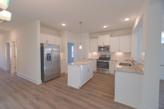 kitchen featuring stainless steel appliances, a kitchen island, sink, pendant lighting, and white cabinetry