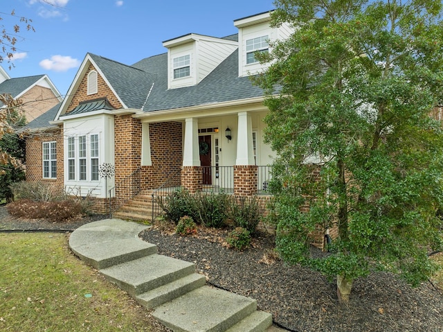 view of front of home featuring brick siding, a porch, and a shingled roof