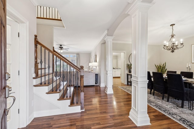 foyer featuring ornate columns, crown molding, dark wood-type flooring, and ceiling fan with notable chandelier