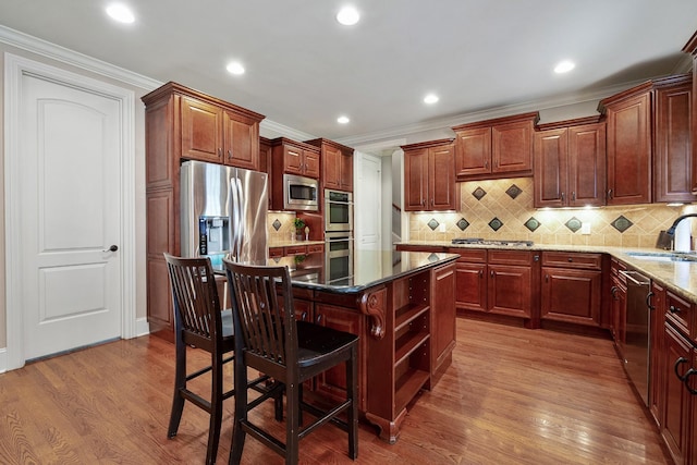 kitchen with hardwood / wood-style floors, dark stone countertops, appliances with stainless steel finishes, a kitchen island, and a kitchen bar