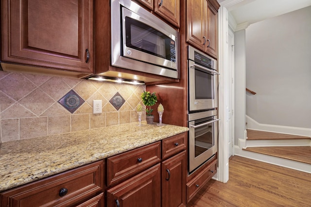 kitchen featuring decorative backsplash, light stone countertops, ornamental molding, stainless steel appliances, and light hardwood / wood-style floors