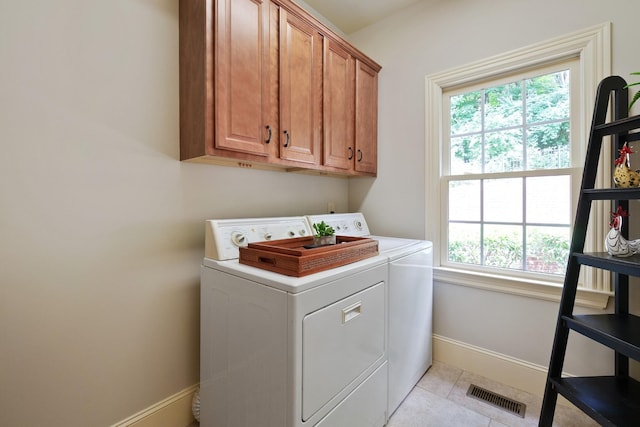 clothes washing area featuring cabinets, light tile patterned floors, and washer and clothes dryer