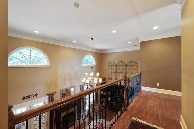 hall with a chandelier, wood-type flooring, a wealth of natural light, and ornamental molding