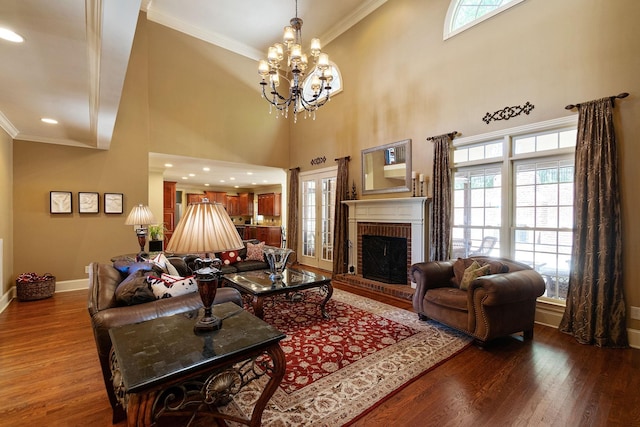 living room featuring a high ceiling, an inviting chandelier, wood-type flooring, a fireplace, and ornamental molding