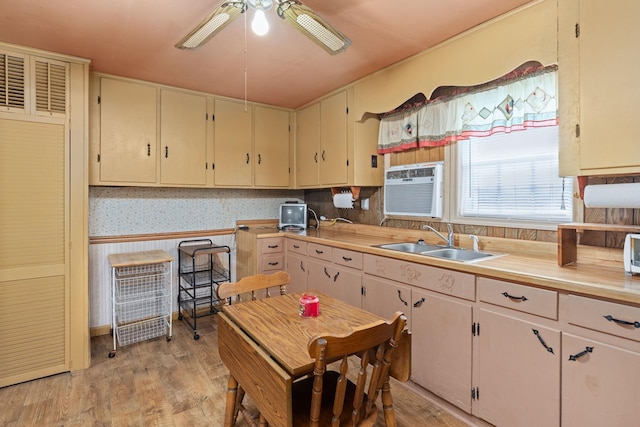 kitchen featuring cream cabinets, sink, light hardwood / wood-style flooring, ceiling fan, and a wall unit AC